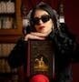 Elegant woman with red lipstick and sunglasses holding 'Nuestra Señora de Paris' book in a luxurious setting.